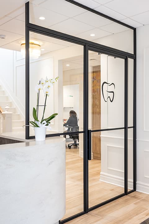 Marble reception desk with white orchid, glass-partitioned entryway, and tooth logo at Endodontie Garofalo