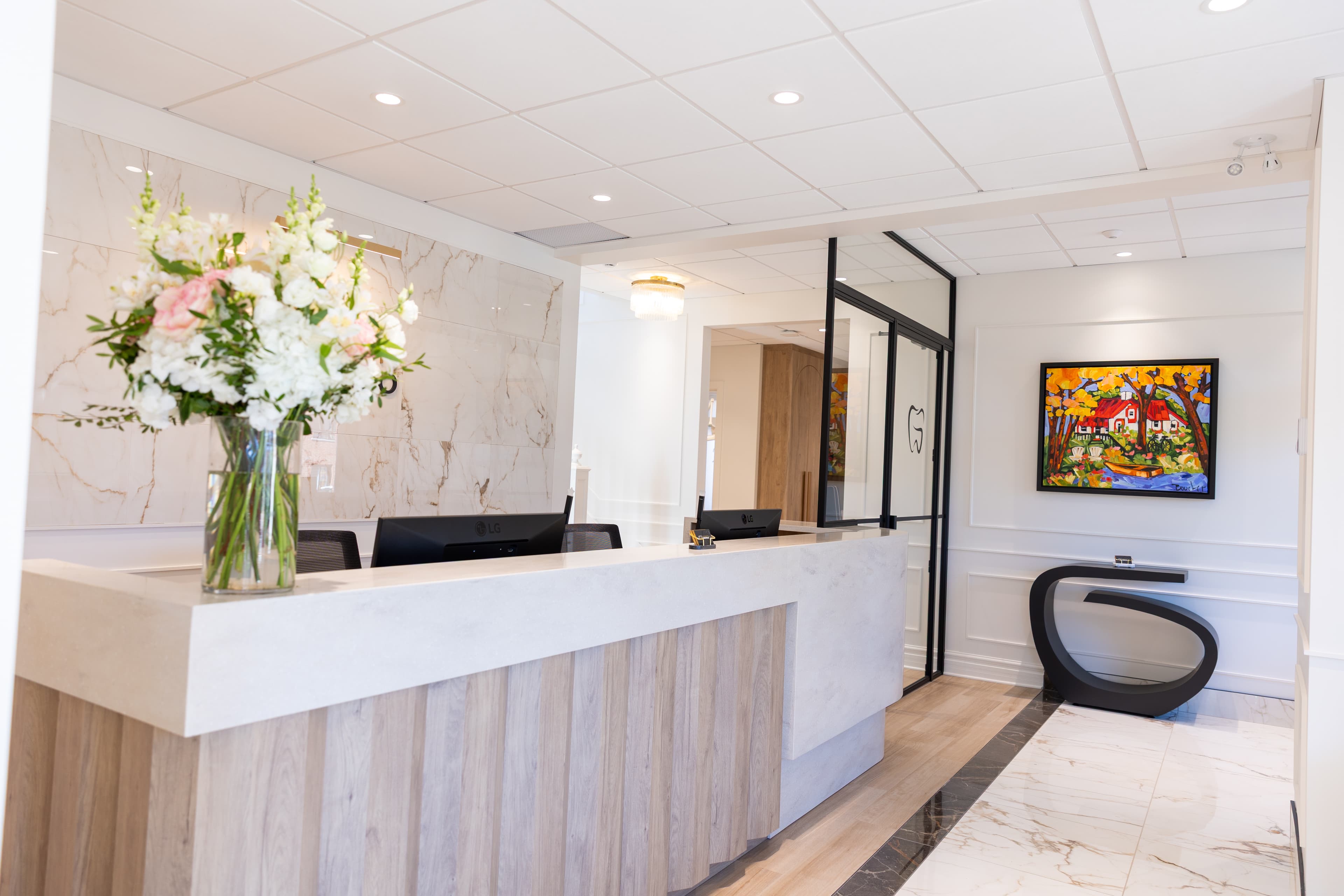 Reception desk with marble wall, floral arrangement, G-shaped console table, and colorful artwork at Endodontie Garofalo