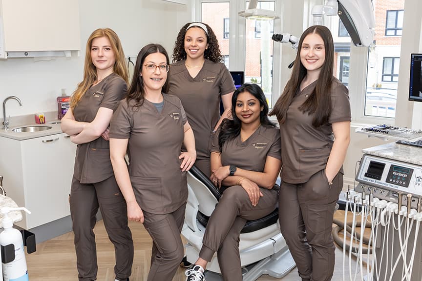Clinical team in taupe scrubs gathered in a modern endodontic treatment room